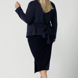 Back view of a size 18 woman wears the Lyndon Jacket in Bluestone. A wrap style jacket with waist belt and collared neckline. Made in soft luxurios modal. Rug up on the way to the office or weekend winter get away. Made in Australia for women size 8 -24.
