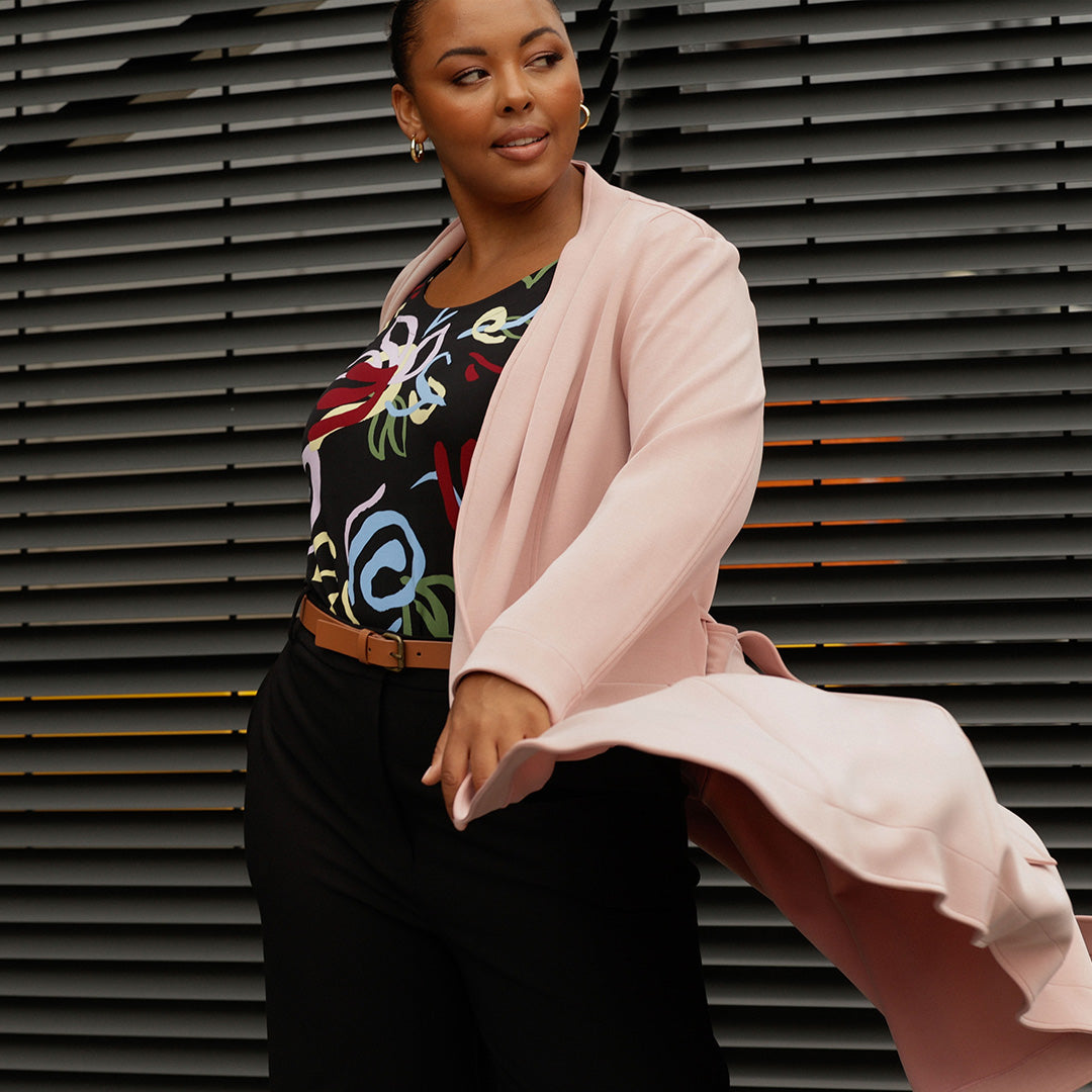 a size 18, plus size woman wears a printed jersey work top with tailored black work pants and a luxurious modal coat in dusty pink, all by Australian-made women's clothing label, Leina & Fleur