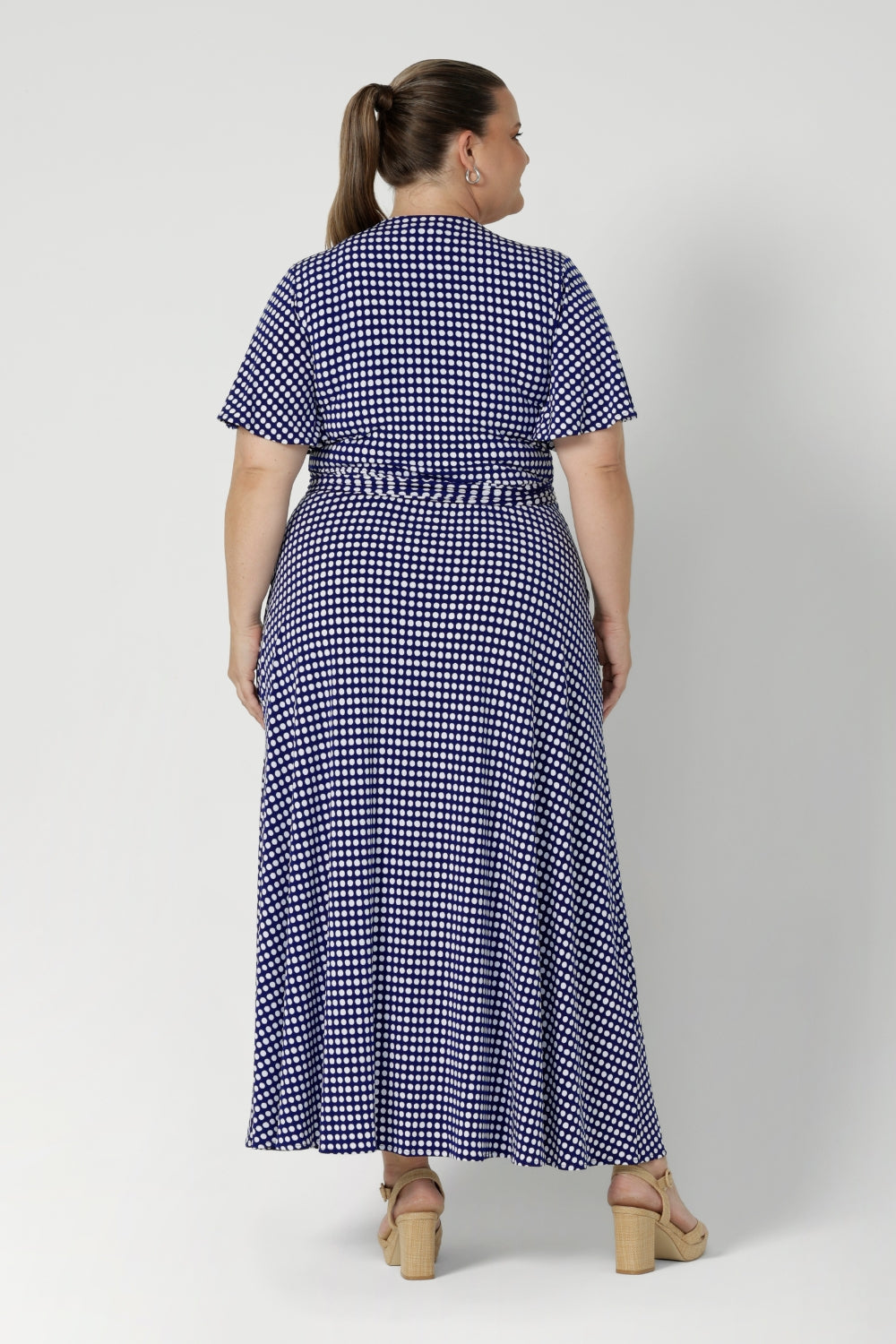 The double-layer back bodice adds subtle structure and interest, while the flutter sleeves create a soft, feminine touch. Plus size model wears navy maxi dress with spotted design.