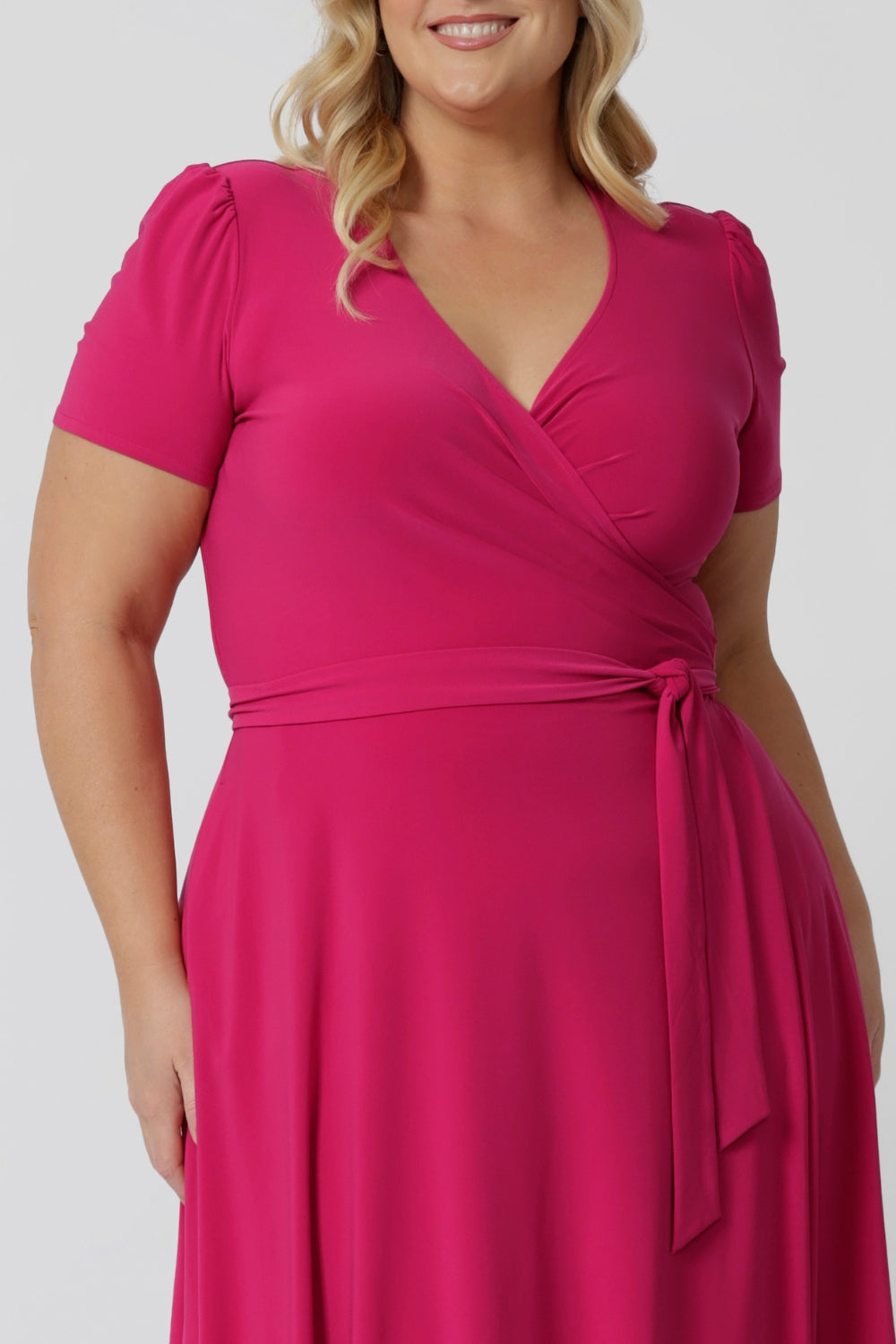 Close up image of a curve model wearing a plus size wrap dress in hot pink. The dress is made in a stretchy jersey by Australian womenswear label Leina & Fleur.