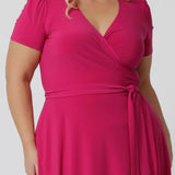 Close up image of a curve model wearing a plus size wrap dress in hot pink. The dress is made in a stretchy jersey by Australian womenswear label Leina & Fleur.