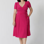 A woman in her thirties wearing a petite height dress in pink. This dress is made by Australian fashion brand Leina & Fleur. 