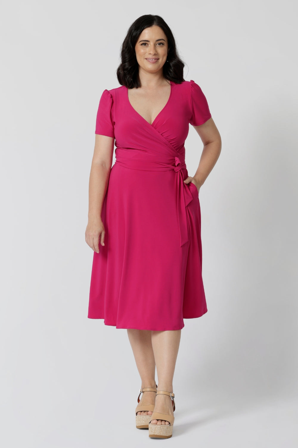 A woman in her thirties wearing a petite height dress in pink. This dress is made by Australian fashion brand Leina & Fleur. 