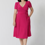 A woman in her thirties wearing a petite height dress in pink. This dress is made by Australian fashion brand Leina & Fleur. 