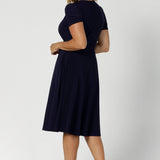 Back view of an over 40, size 12 woman wearing a navy, wrap dress with short sleeves. A great dress for summer casual wear, or for travel. Shop made in Australia dresses in petite to plus sizes online at Australian fashion brand, Leina & Fleur.