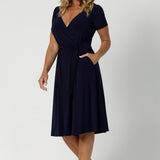 Size 12 woman wears a navy wrap dress with short sleeves. A great dress summer workwear. Shop Australia made dresses in petite to plus sizes at Leina & Fleur in sizes 8-24.