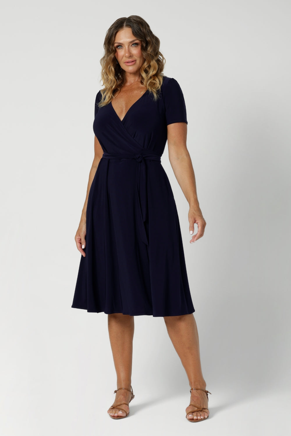 A curvy, size 12 woman wearing a navy, wrap dress with short sleeves. A great dress for summer casual wear, or for travel. Shop made in Australia dresses in petite to plus sizes online at Australian fashion brand, Leina & Fleur.