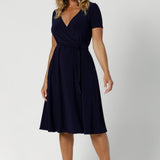 A curvy, size 12 woman wearing a navy, wrap dress with short sleeves. A great dress for summer casual wear, or for back to work. Shop made in Australia dresses in petite to plus sizes online at  fashion brand, Leina & Fleur. Shop Maree Dress in Navy in sizes 8-24.