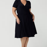 A curvy, size 18 woman wearing a navy, wrap dress with short sleeves. A great dress for summer casual wear, or for travel. Shop made in Australia dresses in petite to plus sizes online at Australian fashion brand, Leina & Fleur.