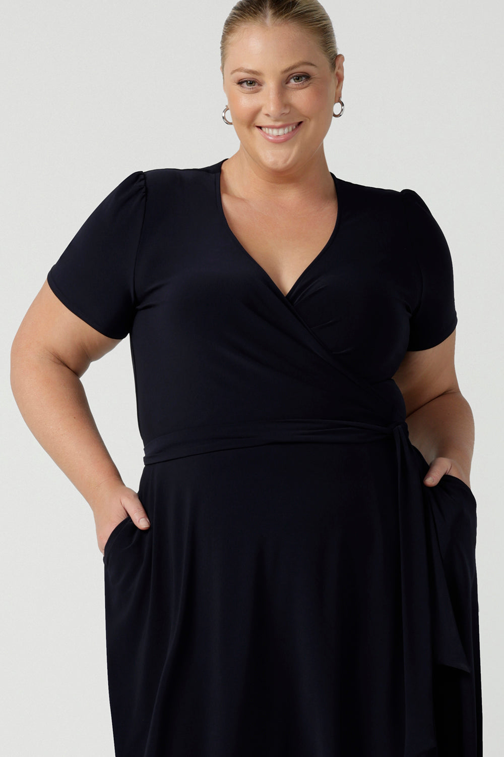 Close up of a curvy, size 18 woman wearing a navy, wrap dress with short sleeves. A great dress for summer casual wear, or for travel. Shop made in Australia dresses in petite to plus sizes online at Australian fashion brand, Leina & Fleur.