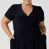 Close up of a curvy, size 18 woman wearing a navy, wrap dress with short sleeves. A great dress for summer casual wear, or for travel. Shop made in Australia dresses in petite to plus sizes online at Australian fashion brand, Leina & Fleur.