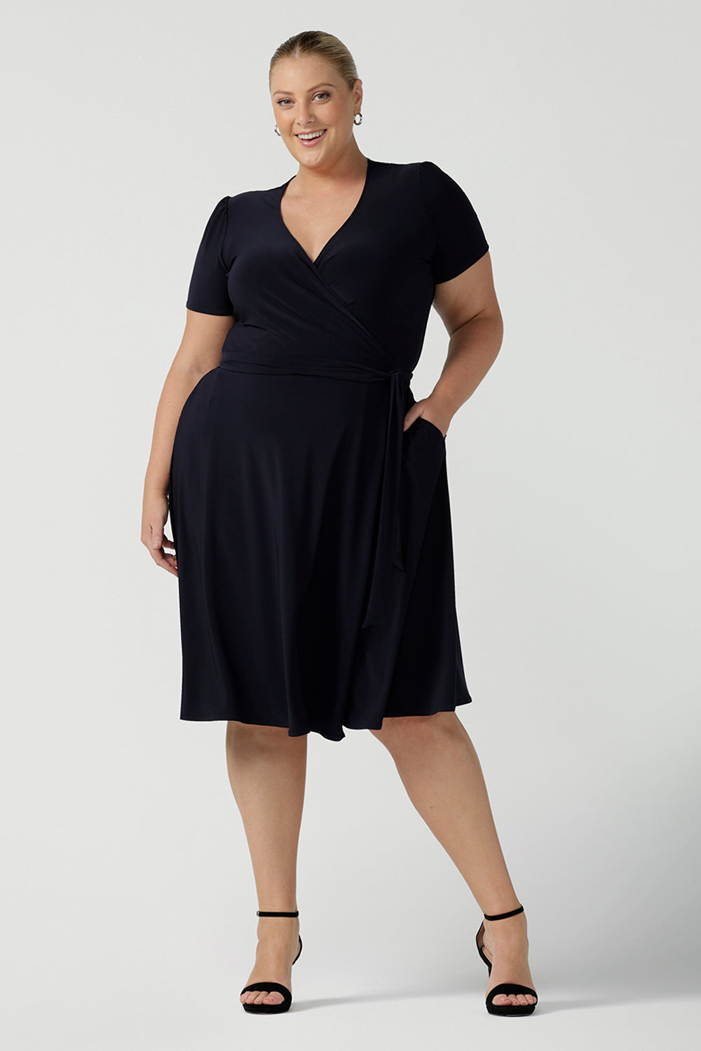 A curvy, size 18 woman wearing a navy, wrap dress with short sleeves. A great dress for summer casual wear, or for travel. Shop made in Australia dresses in petite to plus sizes online at Australian fashion brand, Leina & Fleur.