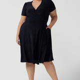 A curvy, size 18 woman wearing a navy, wrap dress with short sleeves. A great dress for summer casual wear, or for travel. Shop made in Australia dresses in petite to plus sizes online at Australian fashion brand, Leina & Fleur.