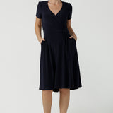  An over 40, size 10 woman wearing a navy, wrap dress with short sleeves. A great dress for summer casual wear, or for travel. Shop made in Australia dresses in petite to plus sizes online at Australian fashion brand, Leina & Fleur.