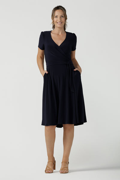  An over 40, size 10 woman wearing a navy, wrap dress with short sleeves. A great dress for summer casual wear, or for travel. Shop made in Australia dresses in petite to plus sizes online at Australian fashion brand, Leina & Fleur.