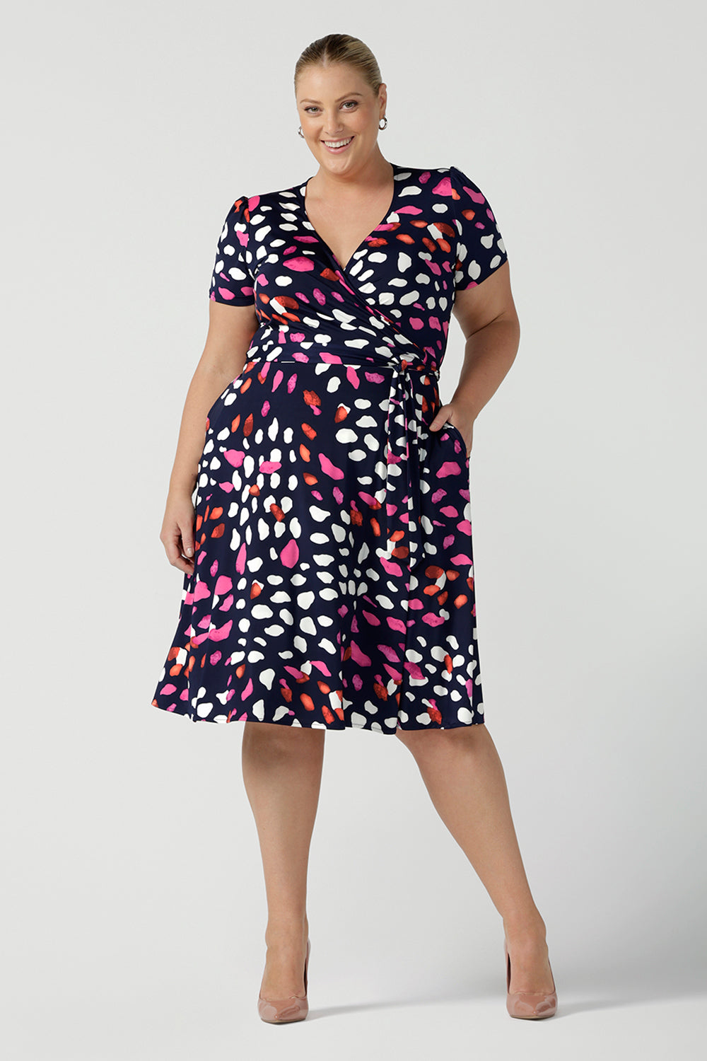 A curvy, size 18 woman wearing a abstract jersey print, knee length wrap dress with short sleeves. A great dress for summer casual wear, or for travel. Shop made in Australia dresses in sizes 8-24 online at Australian fashion brand, Leina & Fleur.