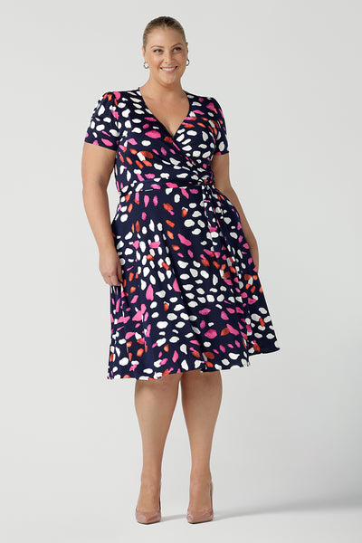 A curvy, size 18 woman wearing a abstract jersey print, knee length wrap dress with short sleeves. A great dress for summer casual wear, or for travel. Shop made in Australia dresses in sizes 8-24 online at Australian fashion brand, Leina & Fleur.