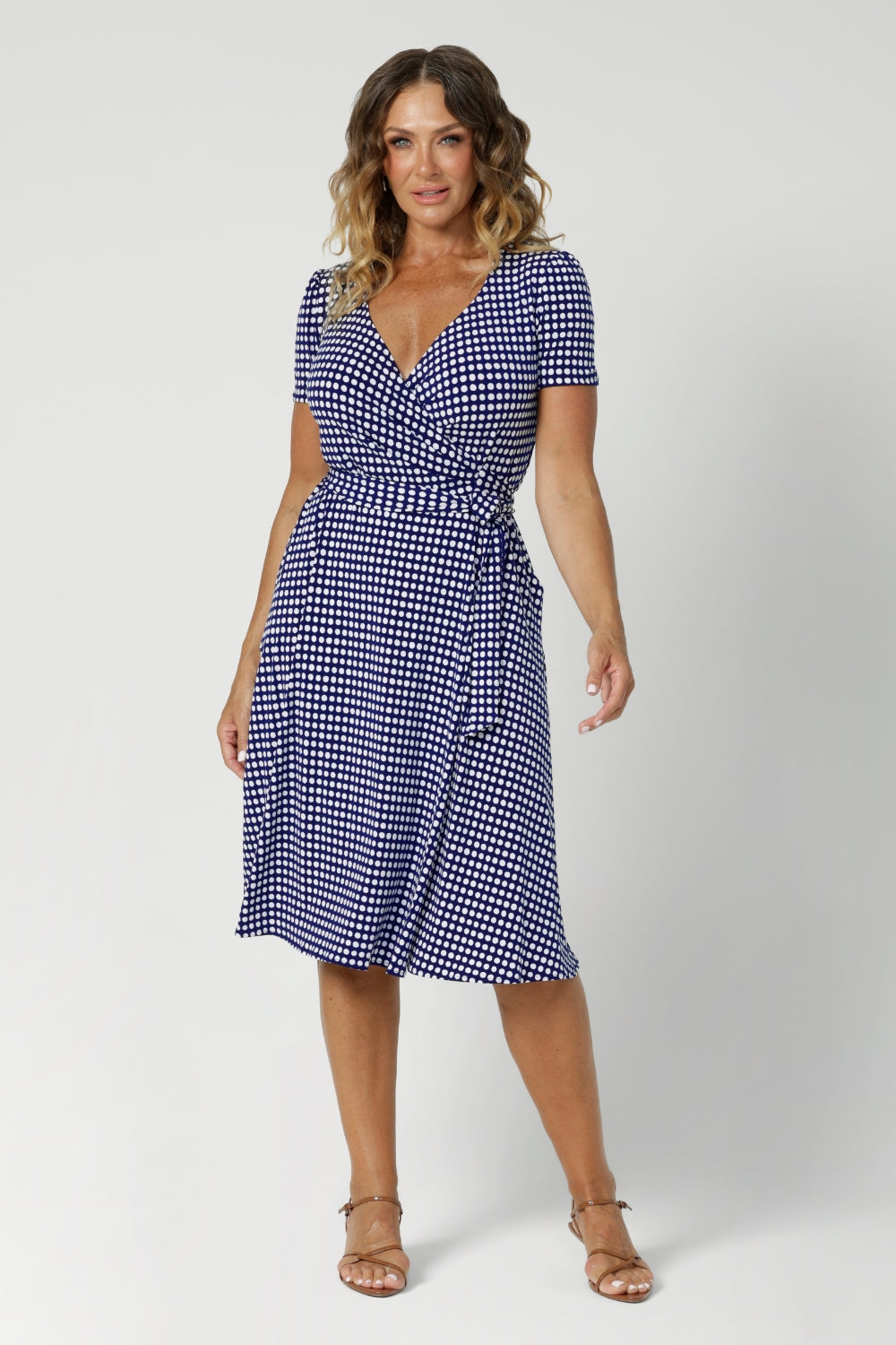 Over 40's woman wears polka dotted wrap dress. Knee length dress features v neckline, fitted short sleeves and aline design. Made from easy care dry touch jersey fabric that is wrinkle resistant. Stocked in sizes 8-24 by Australian made woman's clothing brand Leina & Fleur.