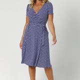 Over 40's woman wears polka dotted wrap dress. Knee length dress features v neckline, fitted short sleeves and aline design. Made from easy care dry touch jersey fabric that is wrinkle resistant. Stocked in sizes 8-24 by Australian made woman's clothing brand Leina & Fleur.