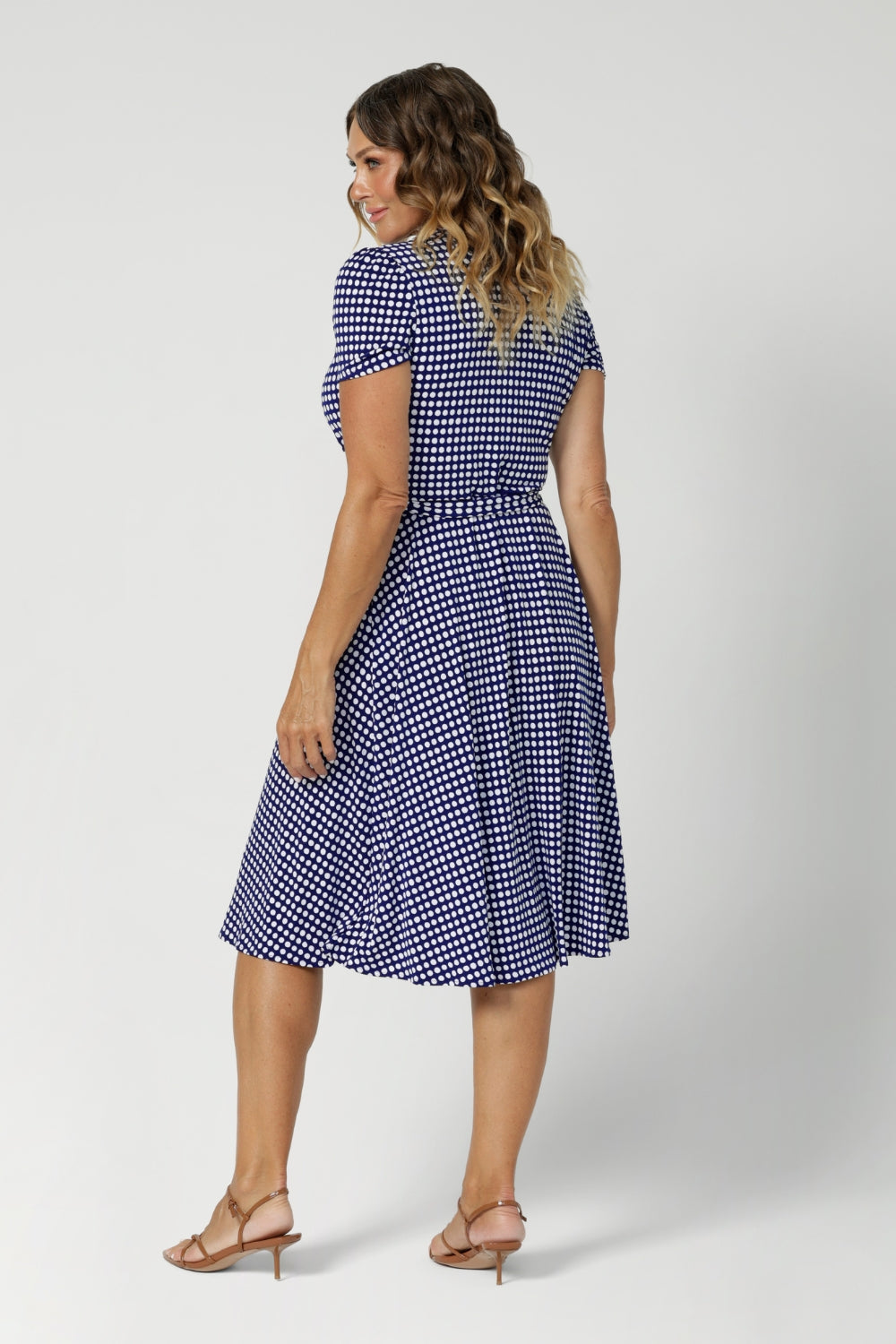 Back view image of size 12 model wearing polka dotted wrap dress. Knee length dress is petite height and plus size friendly, available in sizes across 8-24.  Short sleeve dress features navy polka dot print, wrap design and pockets. Made in Australia from easy care, wrinkle resistant, dry touch jersey fabric. Crafted by woman's clothing brand Leina & Fleur.