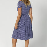 Back view image of size 12 model wearing polka dotted wrap dress. Knee length dress is petite height and plus size friendly, available in sizes across 8-24.  Short sleeve dress features navy polka dot print, wrap design and pockets. Made in Australia from easy care, wrinkle resistant, dry touch jersey fabric. Crafted by woman's clothing brand Leina & Fleur.