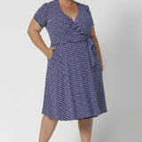 Knee length dress is petite height and plus size friendly, available in sizes across 8-24. Size 18 model wears short sleeve, navy polka dot printed dress with nude heels. Wrap dress is made from wrinkle resistant fabric that is easy care. Made in Australia by woman's clothing brand Leina & Fleur.