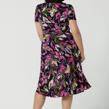 Back view of a size 10 woman wears a size 16 woman wears the Maree dress in Vivid Flora. Short sleeve functioning wrap dress. Knee length dress great for petite heights. Work corporate to weekend wear. Travel friendly. Made in Australia for women size 8 - 24.