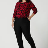 Size 18 woman wears the Mason top in Bold Poppy . A long sleeve jersey top for women with red floral on a black base. Comfortable work top for women size 8 - 24. Soft jersey fabric and made in Australia for women. Styled back with Black Brooklyn slim fit pants and black heels. 