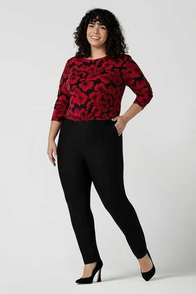 Size 18 woman wears the Mason top in Bold Poppy . A long sleeve jersey top for women with red floral on a black base. Comfortable work top for women size 8 - 24. Soft jersey fabric and made in Australia for women. Styled back with Black Brooklyn slim fit pants and black heels. 