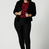 Size 18 woman wears the Mason top in Bold Poppy . A long sleeve jersey top for women with red floral on a black base. Comfortable work top for women size 8 - 24. Soft jersey fabric and made in Australia for women. Styled back with Black Brooklyn slim fit pants and black heels and Garcia ponte jacket.