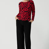 Size 10 woman wears the Mason top in Bold Poppy . A long sleeve jersey top for women with red floral on a black base. Comfortable work top for women size 8 - 24. Soft jersey fabric and made in Australia for women. Styled back with the Monroe pant in black a straight leg pant. 