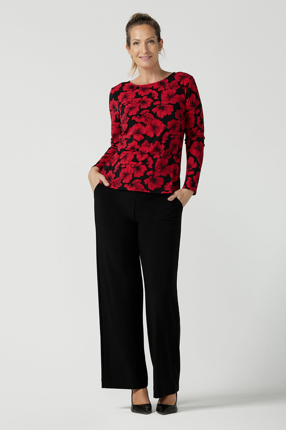 Size 10 woman wears the Mason top in Bold Poppy . A long sleeve jersey top for women with red floral on a black base. Comfortable work top for women size 8 - 24. Soft jersey fabric and made in Australia for women. Styled back with the Monroe pant in black a straight leg pant. 