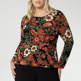 Size 18 woman wears Mason Top in Tapestry, a black base with rich shades of red, orange, pink, beige, and green. Perfect Top for layering as the weather cools, with its chic boat neckline and clean, streamlined design. Available in size 8-24.