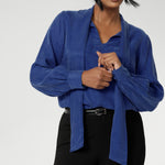 The Matisse Shirt in Cobalt is a pull-on style with a tie neckline, crafted from soft, fluid fabric. Blouson sleeves and buttoned cuffs add a polished finish.