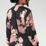 Crafted from a soft, fluid satin rayon fabric, this semi-fitted shirt features a pull-on design with a graceful V-neckline and extended neck ties that can be styled in multiple ways. The romantic floral print blooms across a black satin base, with delicate pink tones adding depth and softness to the look.