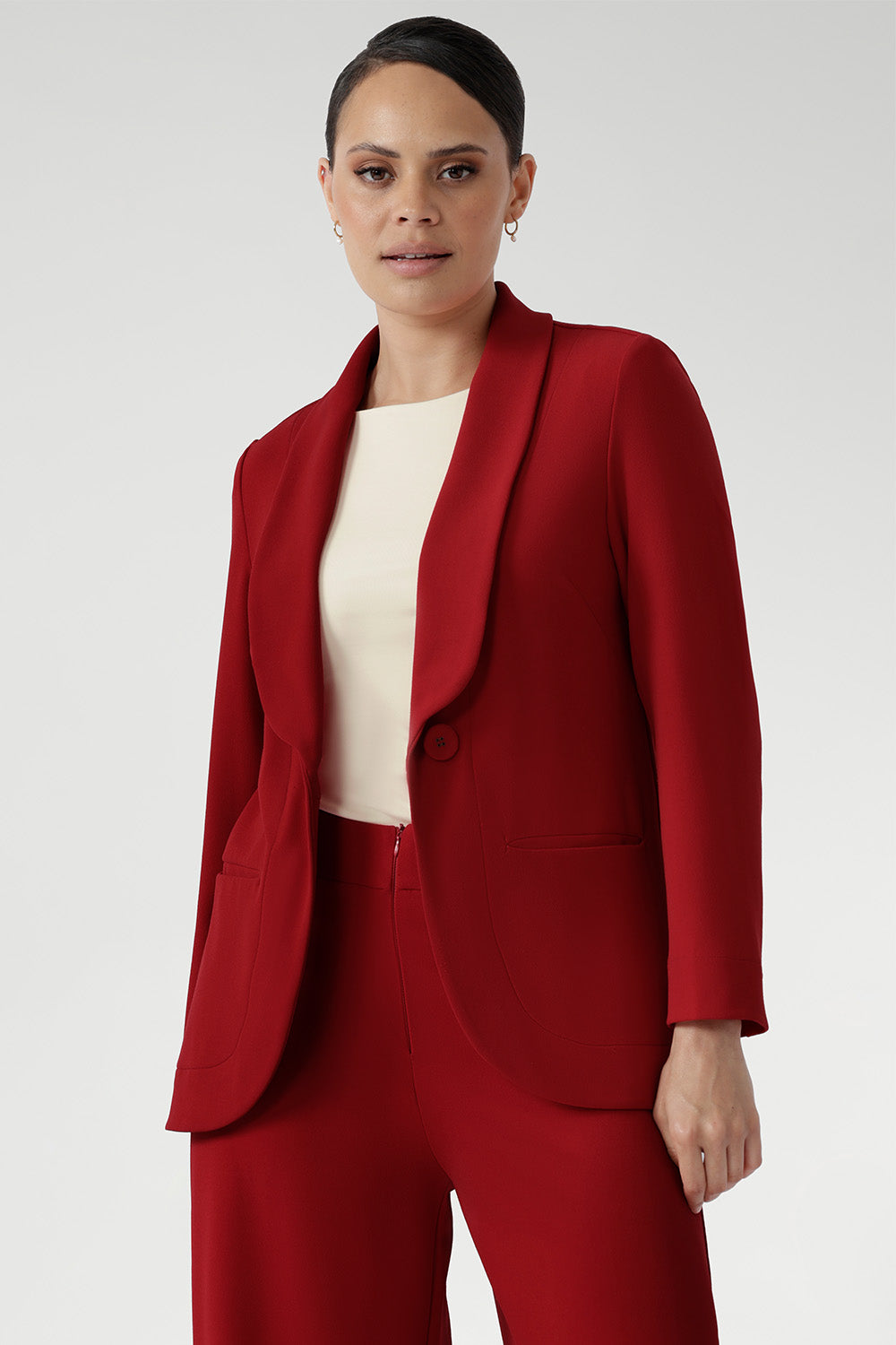 Plus size woman wears the Merit Blazer in Flame, a textured scuba crepe blazer with button front. This red work blazer is worn with red workwear pants and red cami top. Curved hemline and front pockets. Made in Australia for women size 8 - 24.