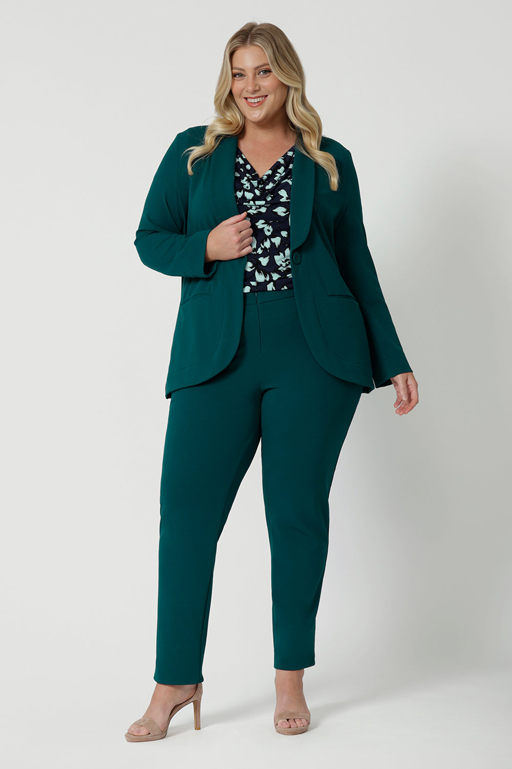 Showing a good work blazer for plus size women, a size 18 woman wears a longline, green blazer with pockets. Worn with a navy print top and tapered leg green workwear pants, this soft suiting is perfect for work and corporate wear. Made in Australia by Australian and New Zealand women's clothing brand, Leina & Fleur, shop work blazers in plus size to petite height in their online boutique.