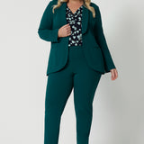 Showing a good work blazer for plus size women, a size 18 woman wears a longline, green blazer with pockets. Worn with a navy print top and tapered leg green workwear pants, this soft suiting is perfect for work and corporate wear. Made in Australia by Australian and New Zealand women's clothing brand, Leina & Fleur, shop work blazers in plus size to petite height in their online boutique.