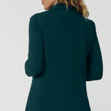 Back view of a good work blazer for over 50s women . A size 12 woman wears a longline, green blazer with pockets. Worn with wide leg green workwear pants, this stretch jacket  is perfect for work and corporate wear. Made in Australia by Australian and New Zealand women's clothing brand, Leina & Fleur, shop work blazers in plus size to petite height in their online boutique.