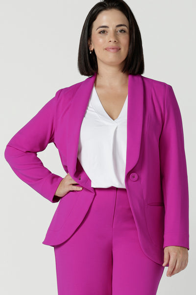 Size 10 woman wears a fuchsia Merit Blazer in scuba crepe.  Tailored design with self covered buttons, shawl collar and curved hem and pockets. Size inclusive for stylish corporate workwear for women. Size 8 - 24. 