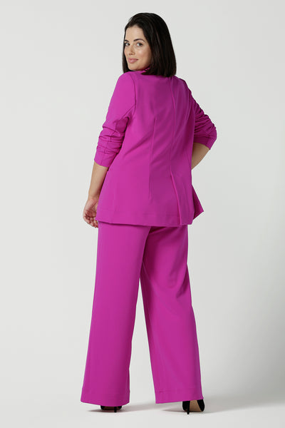Back view of a size 10 woman wears a fuchsia Merit Blazer in scuba crepe. Tailored design with self covered buttons, shawl collar and curved hem and pockets. Size inclusive for stylish corporate workwear for women. Size 8 - 24.