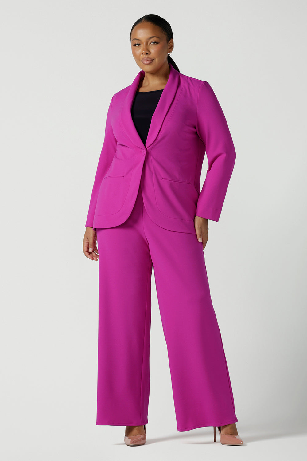 Size 16 woman wears a fuchsia Merit Blazer in scuba crepe. Tailored design with self covered buttons, shawl collar and curved hem and pockets. Size inclusive for stylish corporate workwear for women. Size 8 - 24.
