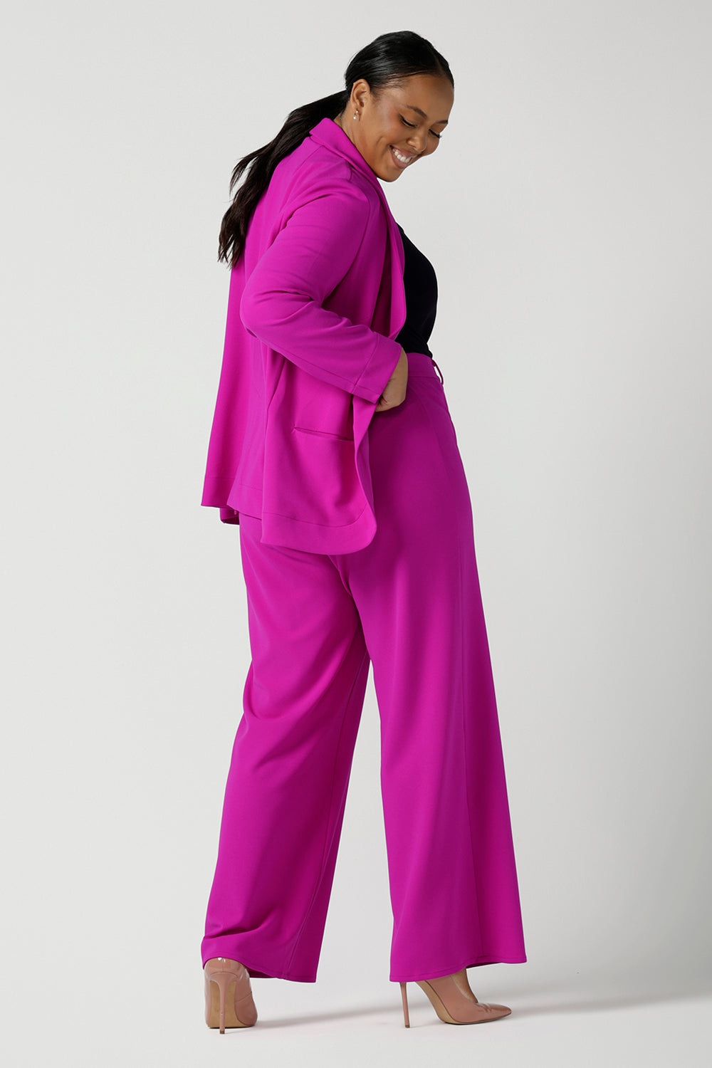 Size 16 woman wears a fuchsia Merit Blazer in scuba crepe. Tailored design with self covered buttons, shawl collar and curved hem and pockets. Size inclusive for stylish corporate workwear for women. Size 8 - 24.