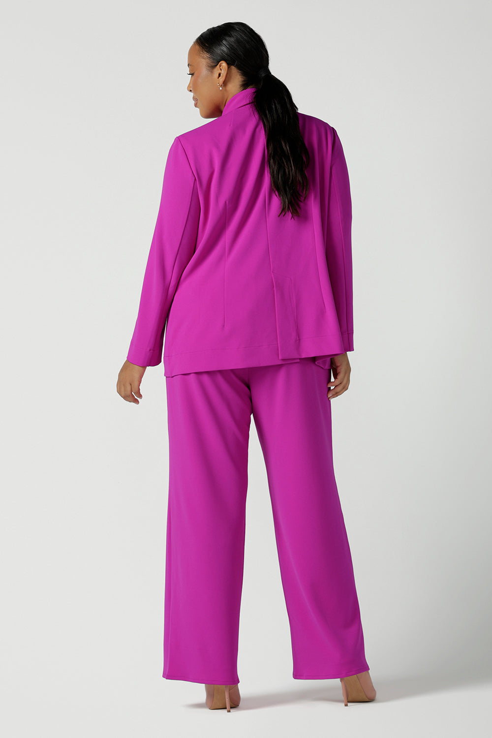 Back view of a size 16 woman wears a fuchsia Merit Blazer in scuba crepe. Tailored design with self covered buttons, shawl collar and curved hem and pockets. Size inclusive for stylish corporate workwear for women. Size 8 - 24.