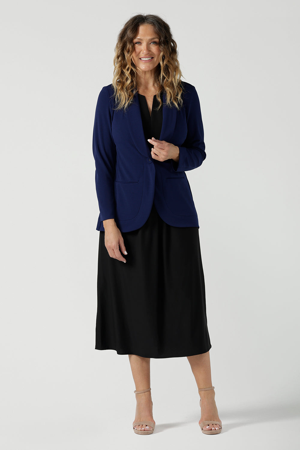 A size 10 woman wears the Merit Blazer in Sailor Scuba crepe fabric. A softly tailored blazer with lapel collar and full length sleeves. Button front and pockets. Made in Australia for women size 8-24. Styled back with a Fernanda Dress in Black wit a v-neck. 