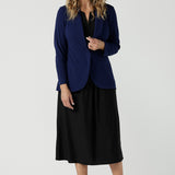 A size 10 woman wears the Merit Blazer in Sailor Scuba crepe fabric. A softly tailored blazer with lapel collar and full length sleeves. Button front and pockets. Made in Australia for women size 8-24. Styled back with a Fernanda Dress in Black wit a v-neck. 