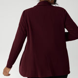 Back view image of Merit Blazer by Leina & Fleur, featured details of pleats and back panels. Tailored woman's blazer is made from easy care fabric in sizes 8-24. Model wears her wine coloured blazer with black workwear pants.