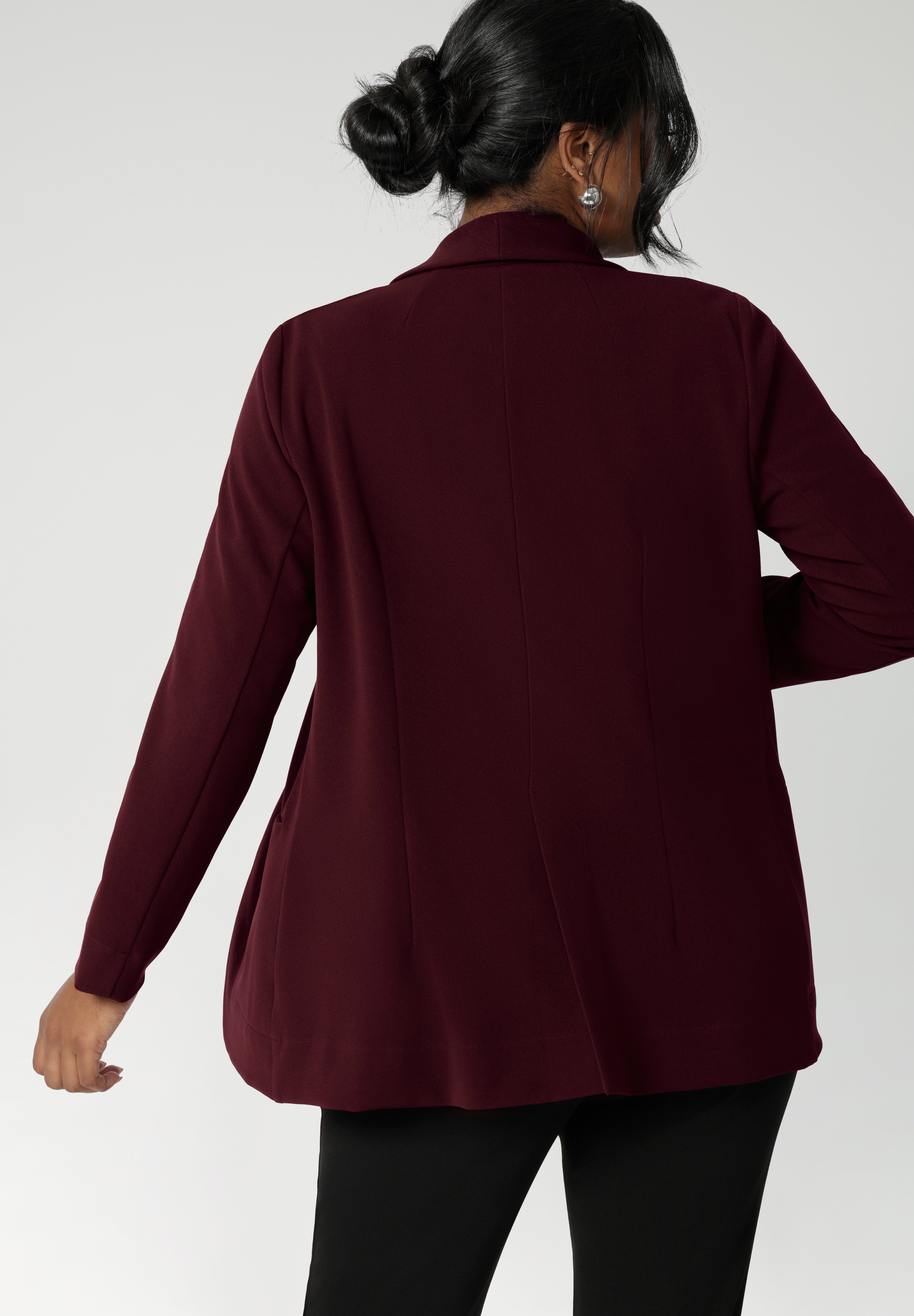 Back view image of Merit Blazer by Leina & Fleur, featured details of pleats and back panels. Tailored woman's blazer is made from easy care fabric in sizes 8-24. Model wears her wine coloured blazer with black workwear pants.