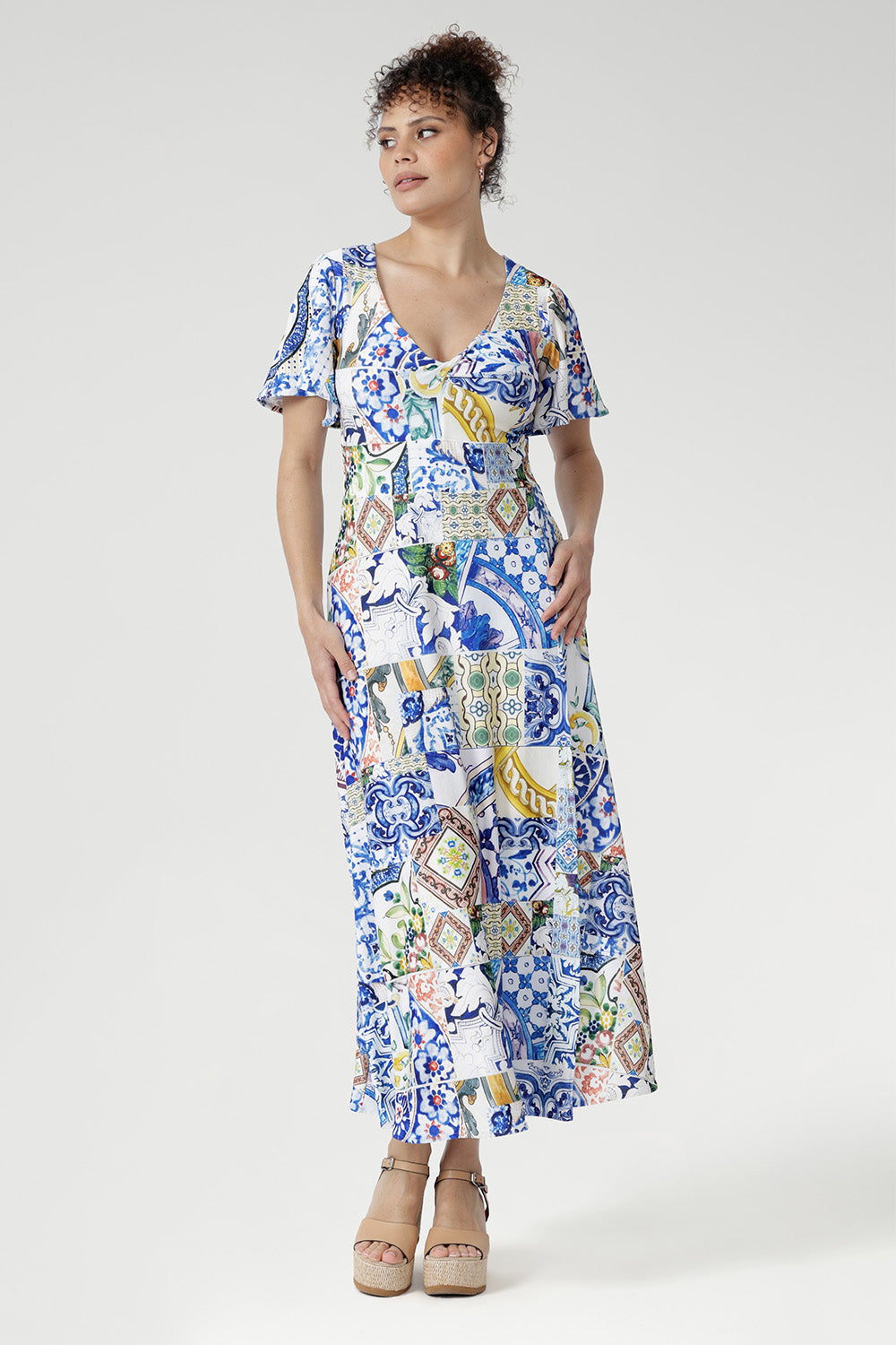 The Sicilian-inspired mosaic print blends shades of cobalt, yellow, brown, and green for a vibrant yet refined aesthetic. With flutter sleeves, a double-layered bodice for comfort and coverage, and a flowing overlap-style maxi skirt, this Australian-made jersey dress is perfect for garden parties, special events, or weddings.