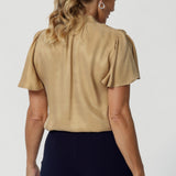 Woven blouse made from luxurious gold soft suede-touch Tencel fabric. This images features a blouse draped beautifully on the body, catching the light in the most flattering way. Though the fabric has no stretch, it offers an effortlessly graceful silhouette that moves with you, creating a striking and sophisticated look. Available in size 8-24.